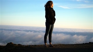 Woman standing triumphantly on top of a tall cliff.