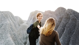 Two young women leaders hiking. One young woman reaches out to help the other.